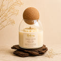 Amber Grove candle by Belora Handcrafts in a glass jar with a cork ball lid, set on a piece of bark