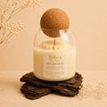 Golden Dusk candle by Belora Handcrafts in a glass jar with a cork ball lid, set on a piece of bark
