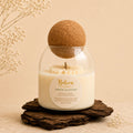 Green Alchemy candle by Belora Handcrafts in a glass jar with a cork ball lid, set on a piece of bark
