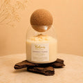 Peppermint Truffle candle by Belora Handcrafts in a glass jar with a cork ball lid, set on a piece of bark