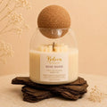 Rose Wood candle by Belora Handcrafts in a glass jar with a cork ball lid, set on a piece of bark