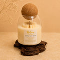 Royal Sea Oud candle by Belora Handcrafts in a glass jar with a cork ball lid, set on a piece of bark