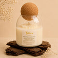 Tropical Bloom candle by Belora Handcrafts in a glass jar with a cork ball lid, set on a piece of bark